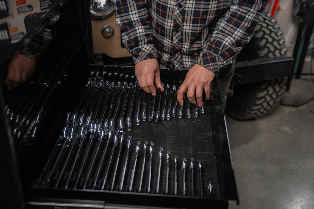 Person organizing a set of wrenches in a drawer with a plaid shirt.