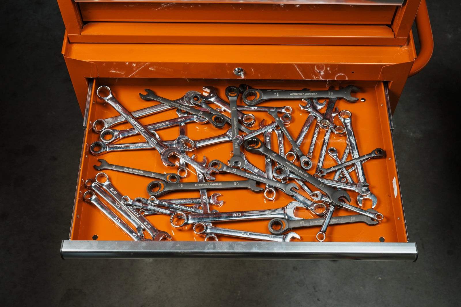 Orange toolbox with a drawer full of wrenches on a dark background